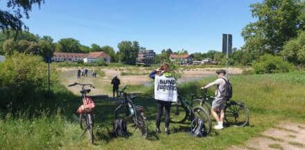 Radfahrer und Wanderer an einem sonnigen Flussufer.