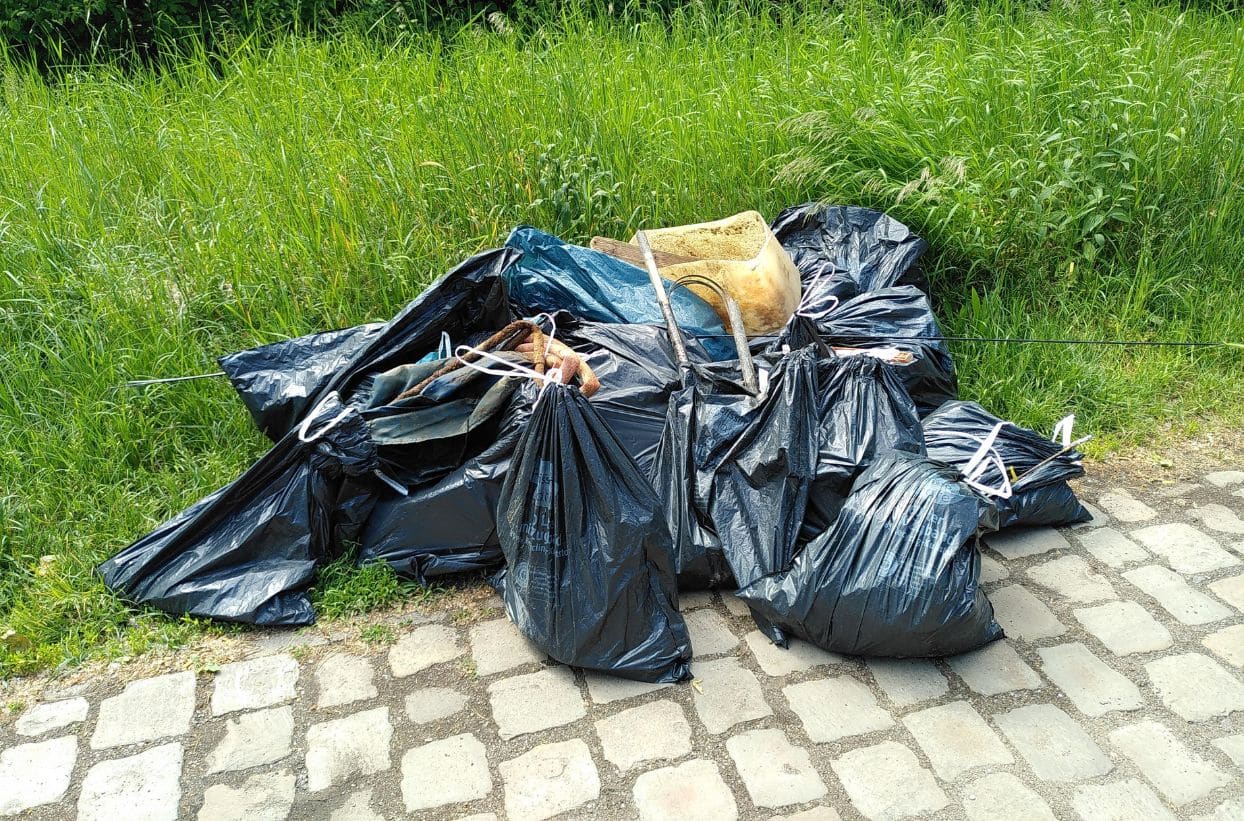 Müllsäcke auf Kopfsteinpflasterweg nahe Wiese