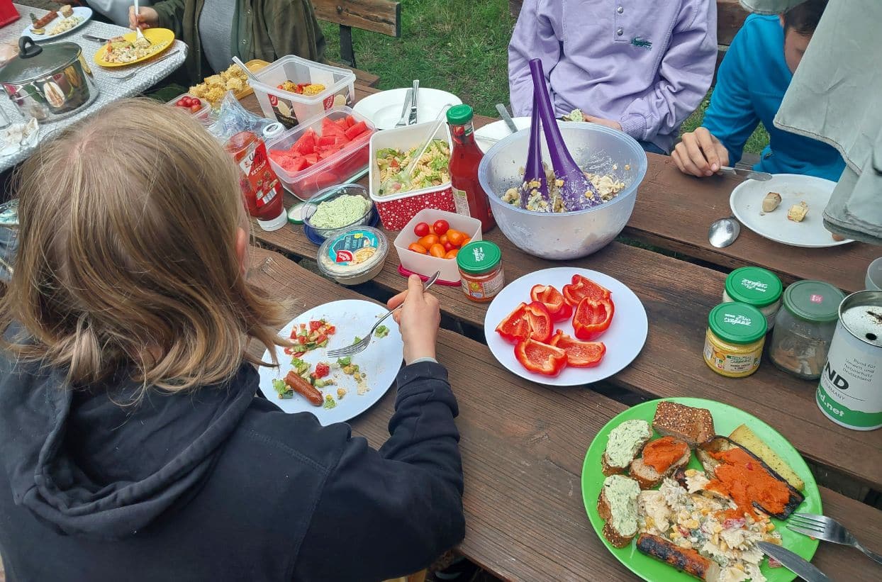 Menschen essen draußen am Tisch mit verschiedenen Speisen.