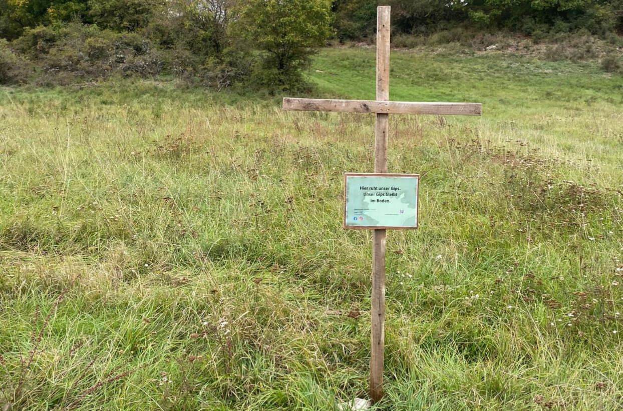 Holzkreuz auf grüner Wiese mit Schild