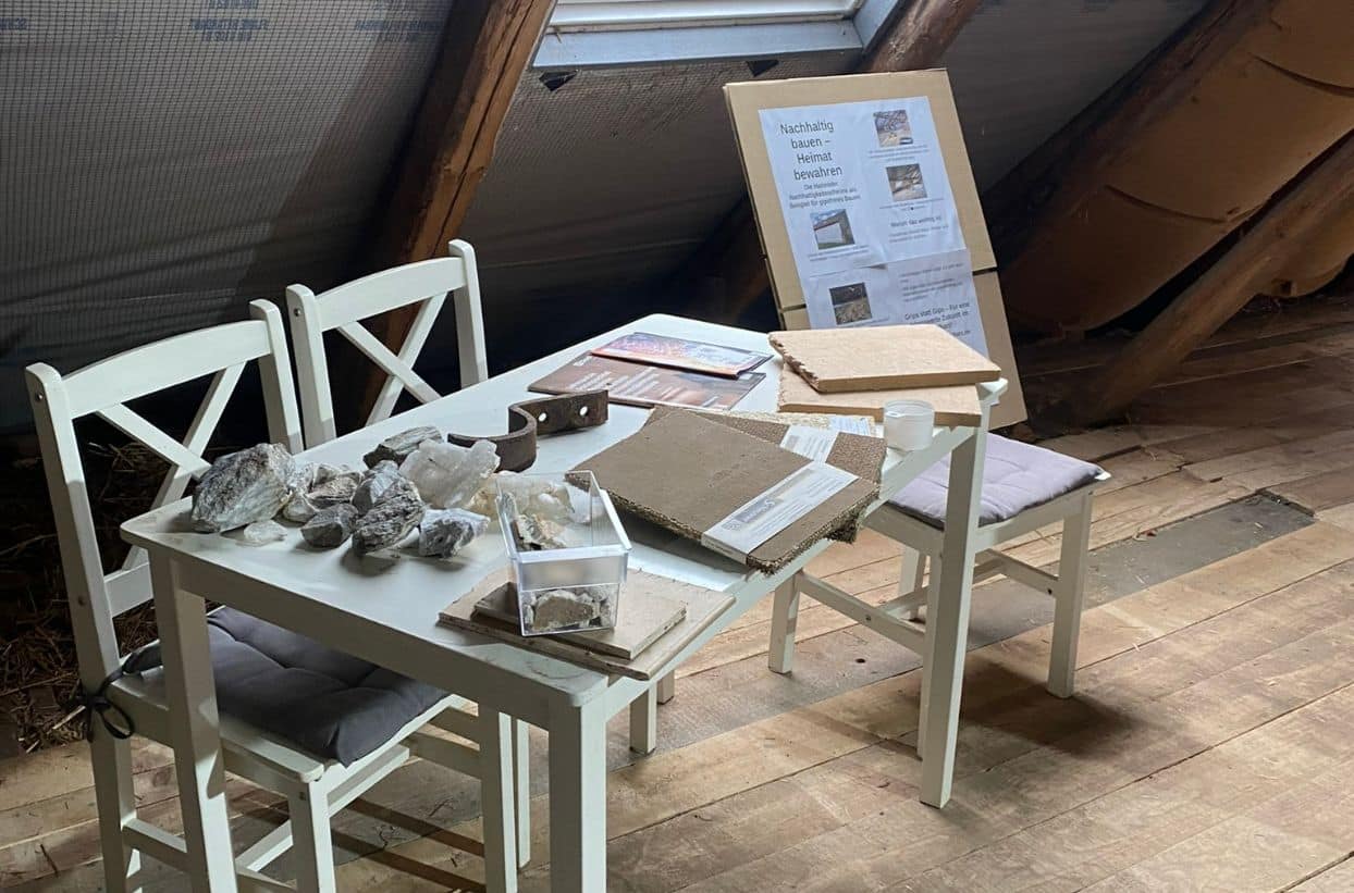 Tisch mit Baumaterialien und Infoplakaten auf Dachboden.